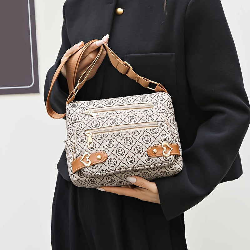 Borsa a tracolla beige con motivo monogramma, dettagli in pelle marrone e chiusure a zip, indossata da una persona in abito nero.