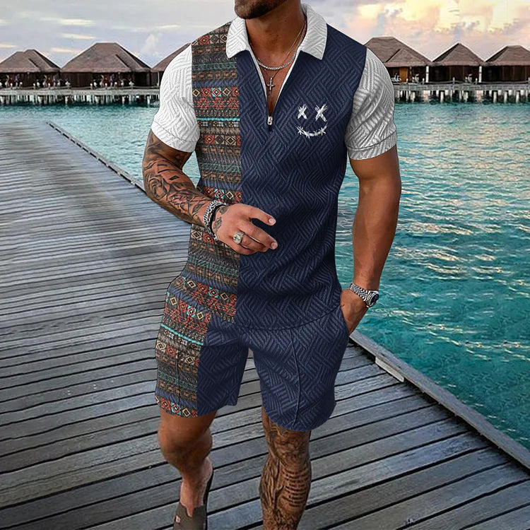 Uomo in tuta estiva a fantasia geometrica e etnica, su passerella di legno vicino al mare, bungalow sullo sfondo. Moda estiva maschile.