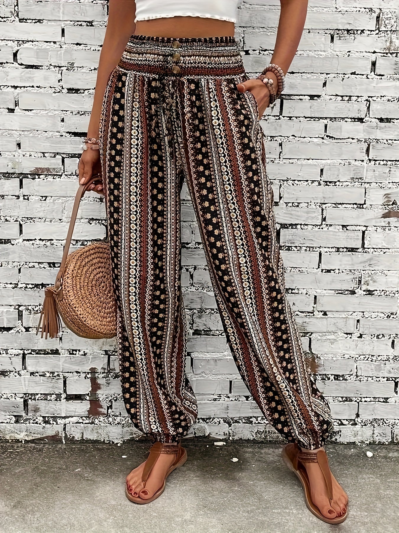 Pantaloni boho a righe etniche, donna, con borsa intrecciata e sandali, moda estiva casual, sfondo muro bianco.