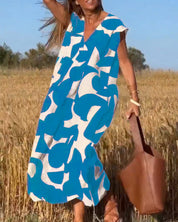 Donna in abito estivo blu e bianco astratto, campo di grano, borsa marrone, giornata soleggiata. Moda estiva, abbigliamento casual.