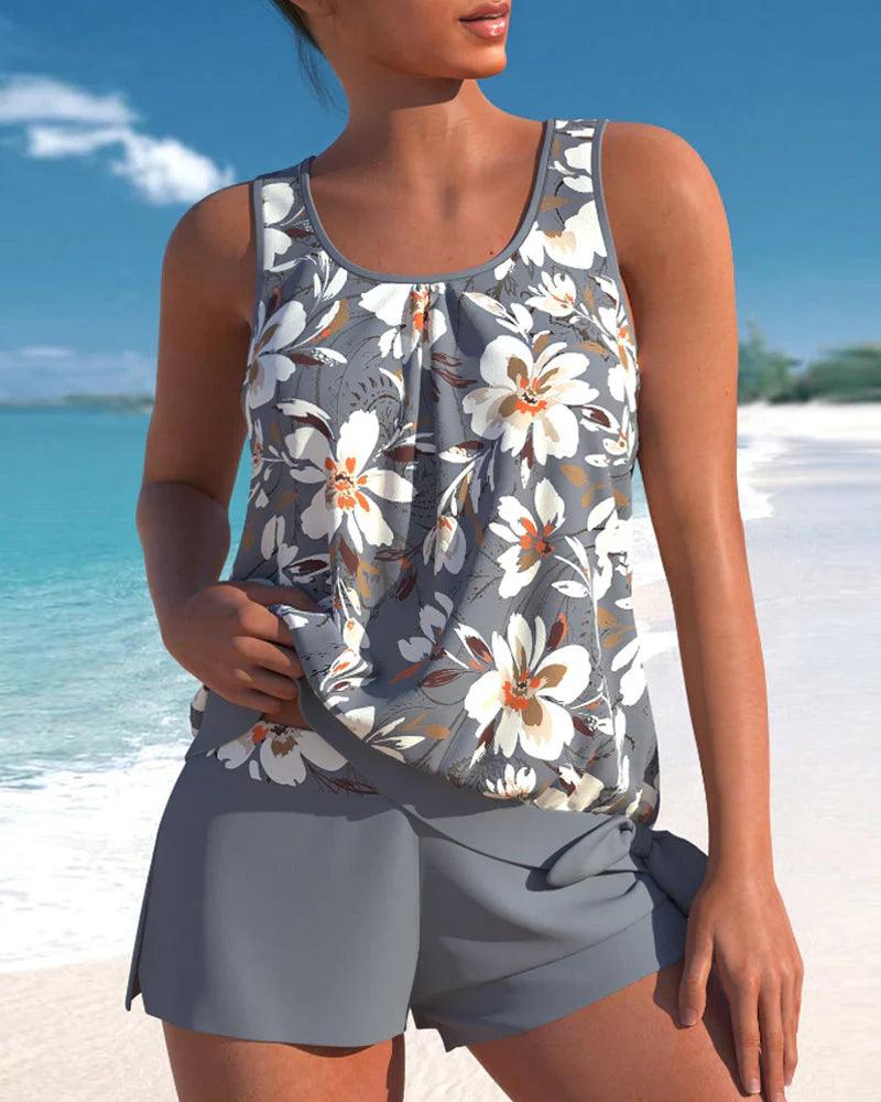 Donna in costume da bagno floreale grigio su spiaggia tropicale. Moda estiva, abbigliamento mare, look vacanza. Sfondo mare e cielo blu.