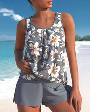 Donna in costume da bagno floreale grigio su spiaggia tropicale. Moda estiva, abbigliamento mare, look vacanza. Sfondo mare e cielo blu.