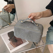 Borsa cosmetica grigia con manico, design elegante, su sedia trasparente. Ideale per viaggi, organizzazione trucco. Accessorio moda pratico e chic.