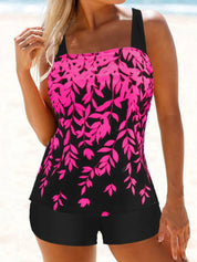 Donna in costume da bagno tankini nero e rosa con motivo floreale, spiaggia sullo sfondo. Moda mare, abbigliamento estivo, costumi da bagno donna.