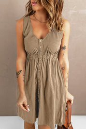 Abito estivo beige senza maniche con bottoni, scollo a V e vita arricciata. Tatuaggi visibili su braccia. Donna con capelli ondulati.