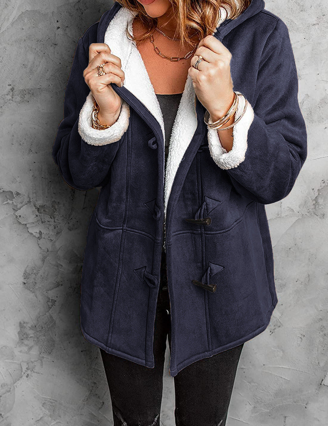 Donna con cappotto invernale blu scuro con fodera in pelliccia sintetica bianca, chiusura a alamari, su sfondo grigio. Moda femminile, abbigliamento caldo.