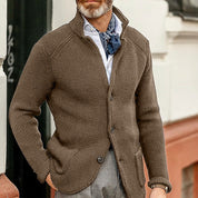 Giacca cardigan uomo marrone, tessuto a maglia, abbinata a camicia bianca e foulard blu. Moda autunnale elegante e casual.