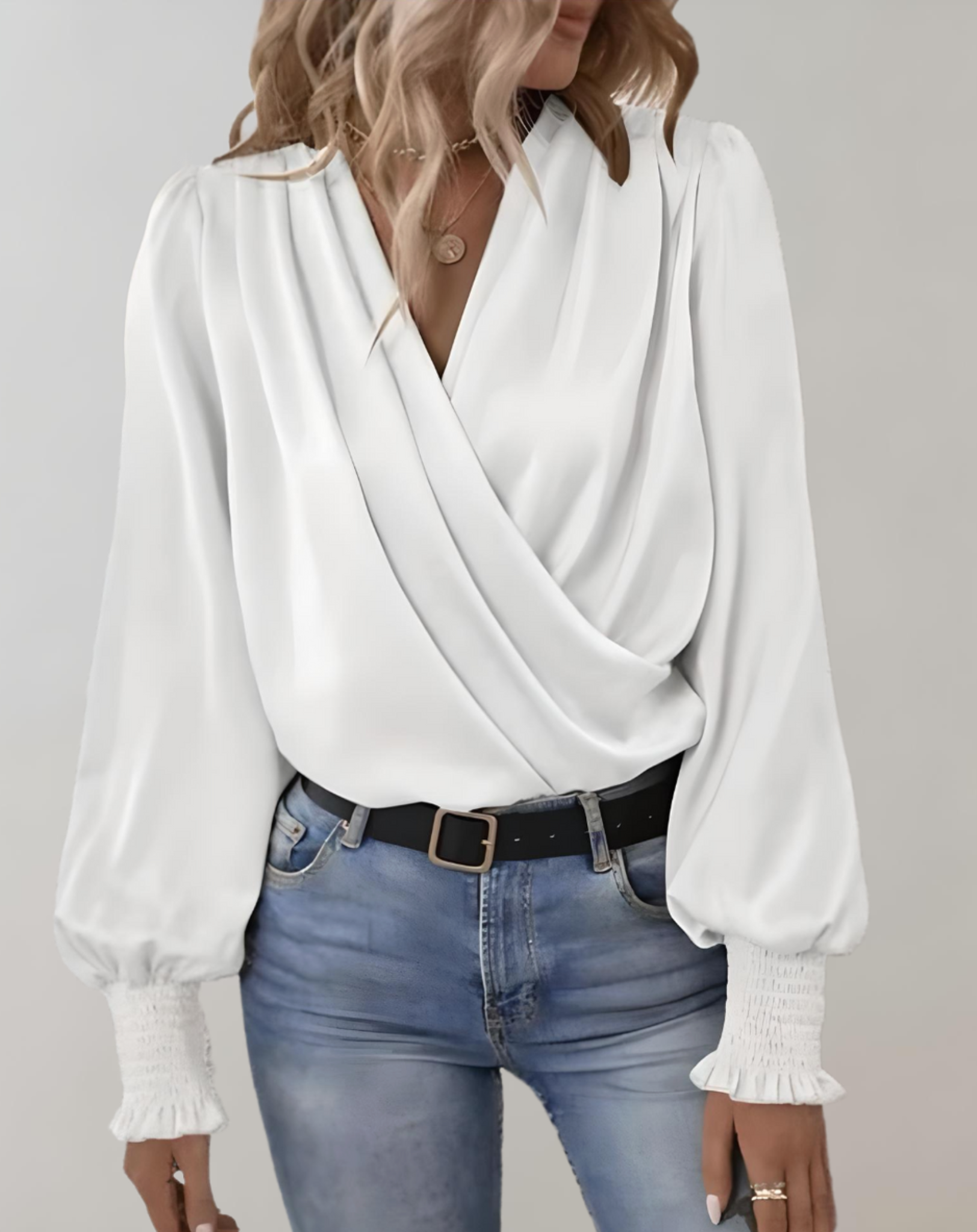 Blusa bianca elegante con scollo a V incrociato, maniche lunghe a sbuffo, abbinata a jeans chiari e cintura nera. Moda donna casual chic.