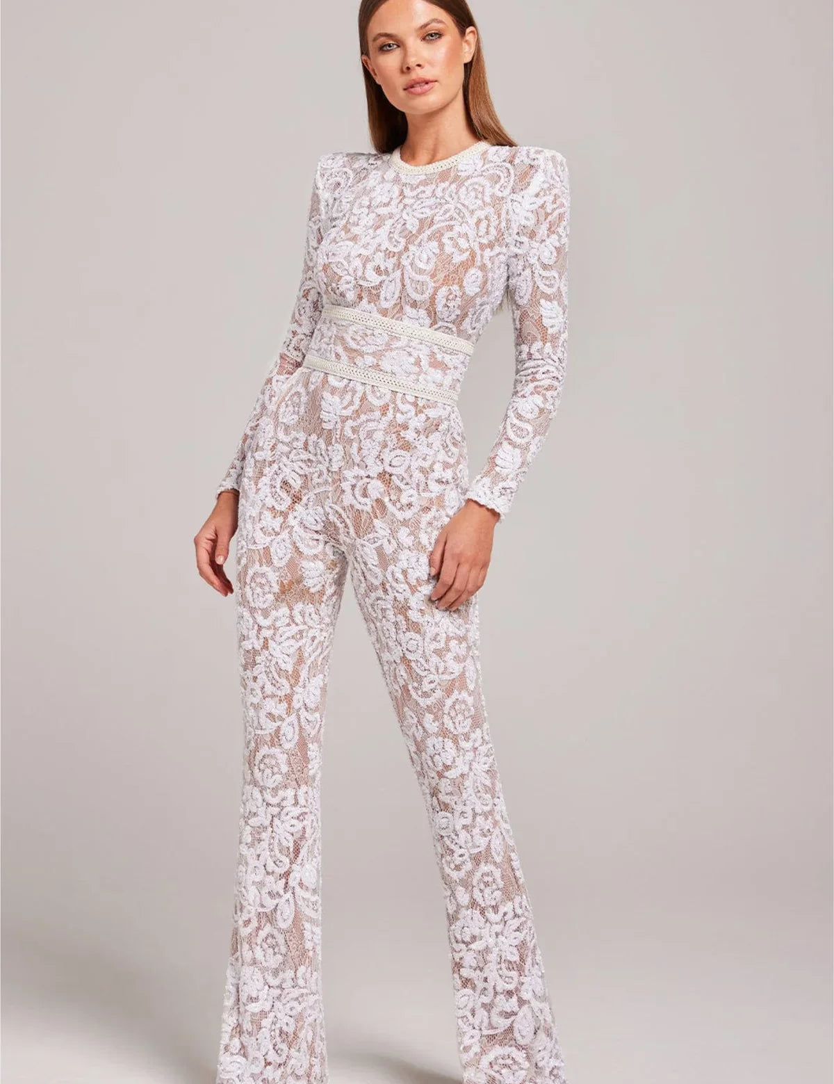Donna in tuta bianca di pizzo trasparente, maniche lunghe, elegante e moderna. Abbigliamento femminile alla moda, ideale per eventi serali.