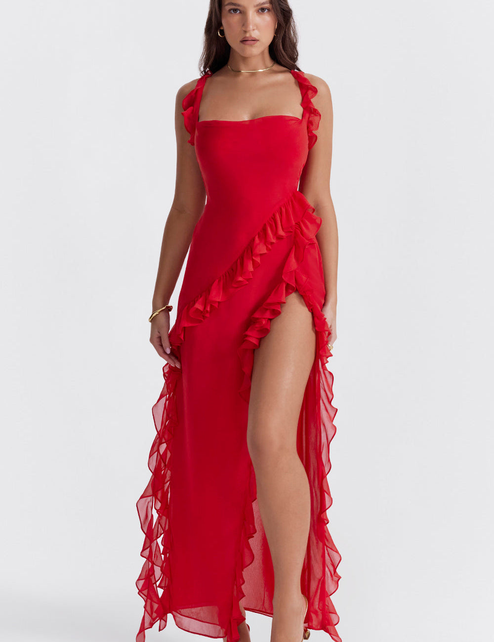 Abito lungo rosso con volant, spacco alto e spalline, indossato da una donna. Elegante e moderno, ideale per eventi serali e cerimonie.