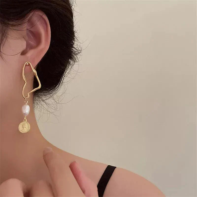 Orecchino pendente dorato con perla e moneta, design moderno, indossato su orecchio femminile. Gioielli eleganti, accessori moda donna.
