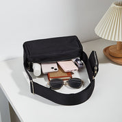 Borsa a tracolla nera su tavolo bianco con occhiali da sole, smartphone, rossetto e lampada. Accessori moda, eleganza, praticità quotidiana.
