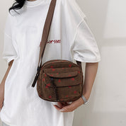 Donna con borsa a tracolla marrone in velluto a coste, motivo floreale rosso, indossa t-shirt bianca. Accessorio moda casual, stile urbano.