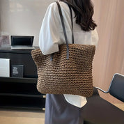 Donna con borsa a tracolla in paglia intrecciata, ufficio moderno, moda sostenibile, accessorio estivo, stile casual chic.