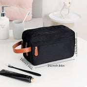 Borsa da toilette nera con manico in pelle marrone, dimensioni 25x15x10 cm, su tavolo da bagno con spazzolino, dentifricio e dispenser sapone.