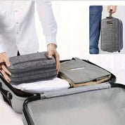 Valigia grigia aperta con organizer da viaggio in tessuto, abbigliamento piegato all'interno, mani che sistemano il contenuto. Ottimizzazione bagaglio.