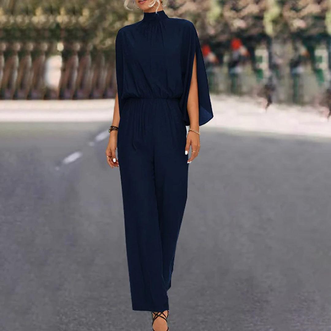 Tuta elegante blu scuro con mantella, donna in strada alberata. Abbigliamento moda femminile, stile sofisticato, tendenza autunno.
