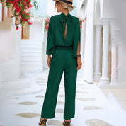 Donna in tuta verde elegante, cappello di paglia, sandali, in strada mediterranea. Moda estiva, abbigliamento casual chic, stile vacanza.