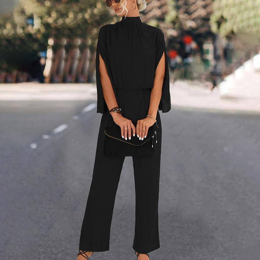 Donna con elegante tuta nera a maniche lunghe, occhiali da sole e borsa a mano, su strada urbana. Moda femminile, abbigliamento chic.