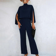 Tuta elegante blu scuro da donna con maniche a mantella, abbinata a borsa nera e sandali. Look sofisticato per eventi formali.