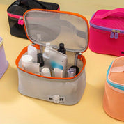 Borsa da toilette in rete grigia aperta con prodotti per la cura personale, circondata da altre borse colorate. Organizzatore da viaggio pratico e spazioso.