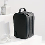 Elegante borsa da toilette nera in pelle sintetica, con doppia cerniera e manico, ideale per viaggi. Accessori bagno sullo sfondo.