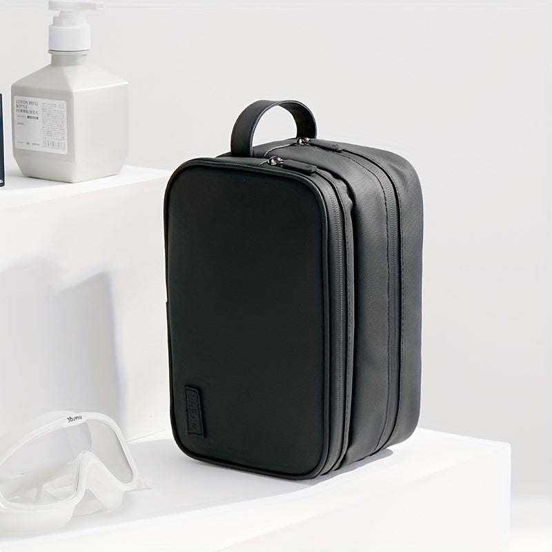 Elegante borsa da toilette nera in pelle sintetica, con doppia cerniera e manico, ideale per viaggi. Accessori bagno sullo sfondo.