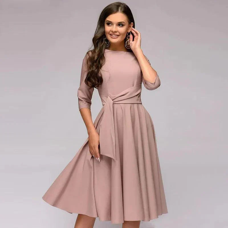 Abito elegante donna rosa, maniche a tre quarti, scollo rotondo, cintura annodata, perfetto per cerimonie e occasioni speciali.
