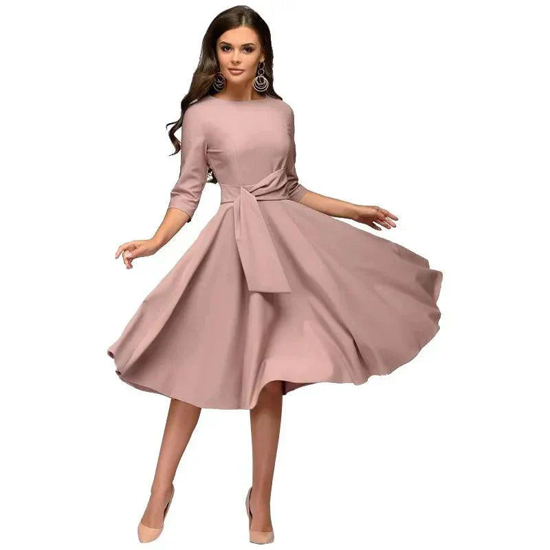Abito elegante donna rosa cipria, maniche a tre quarti, gonna svasata, cintura in vita, perfetto per cerimonie e occasioni speciali.