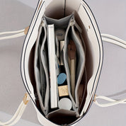 Borsa a mano bianca aperta vista dall'alto, con scomparti organizzati contenenti libri, cosmetici e accessori. Design elegante e funzionale.