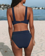 Donna in spiaggia con bikini blu scuro a vita alta, vista posteriore. Costume da bagno estivo, moda mare, stile elegante.