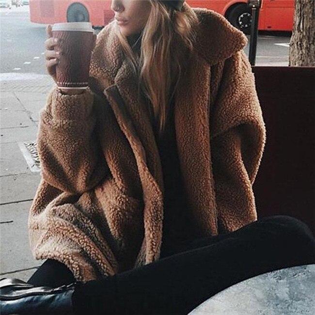 Donna con cappotto teddy bear beige, seduta all'aperto, tiene una tazza di caffè. Moda invernale, stile casual, comfort urbano.