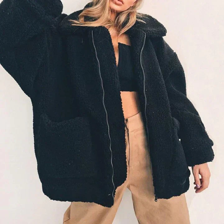 Giacca in pelliccia sintetica nera da donna, oversize, con zip, abbinata a top nero e pantaloni beige. Moda invernale, stile casual chic.
