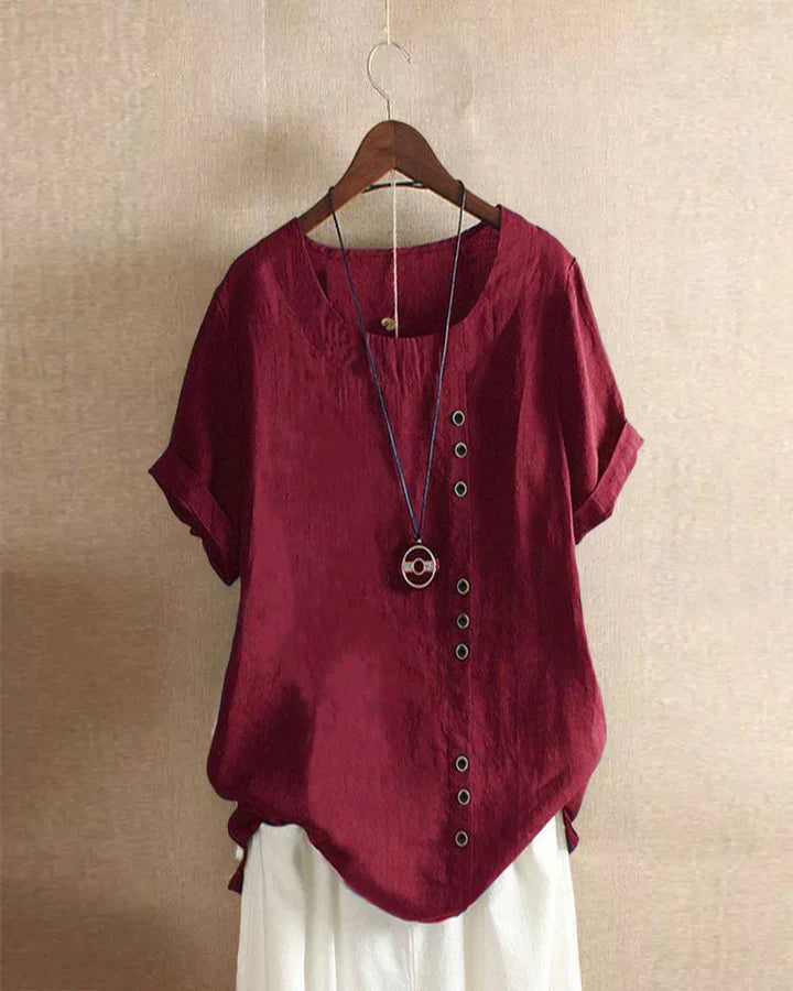 Blusa rossa in lino con bottoni decorativi, maniche corte, scollo rotondo, appesa su gruccia. Moda donna estiva casual elegante.