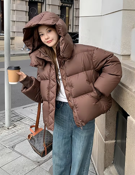 Donna con giacca invernale marrone, jeans larghi, borsa a tracolla e caffè da asporto. Moda urbana, abbigliamento casual, cappotto imbottito.