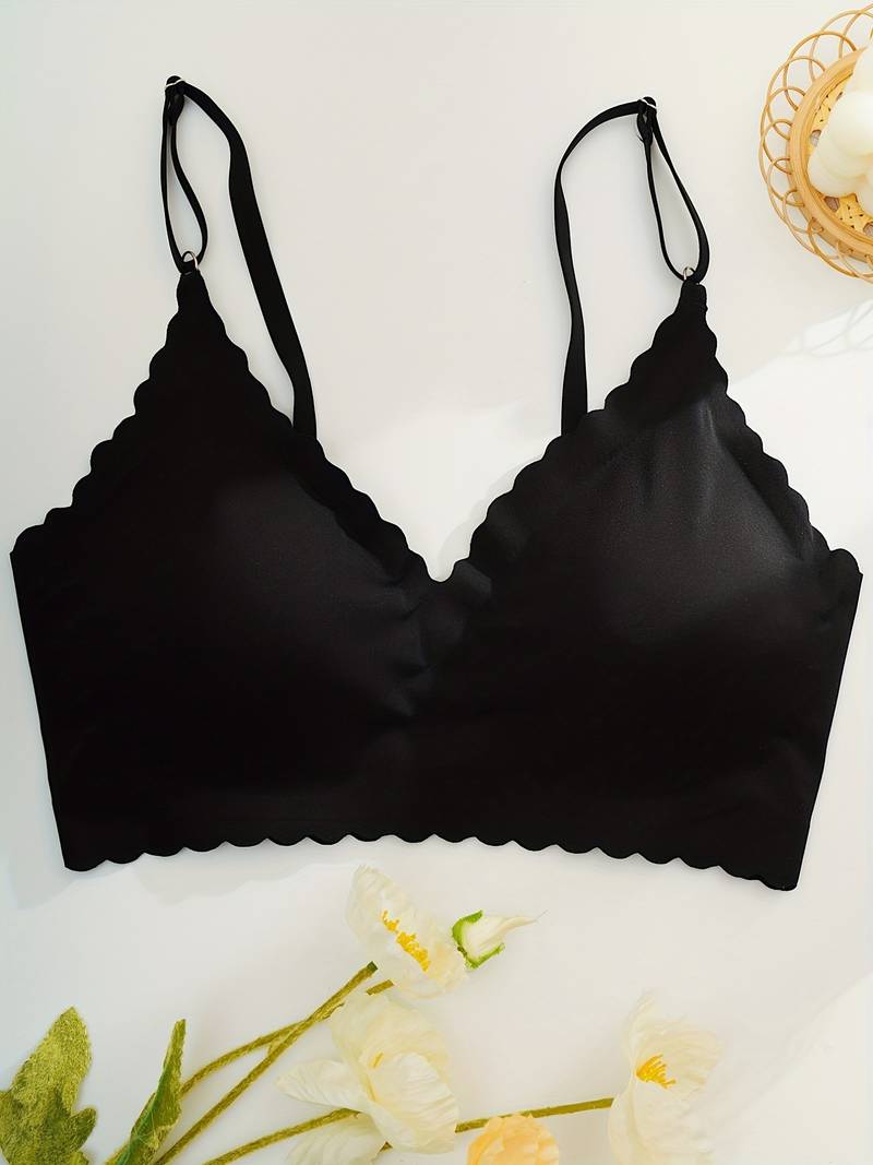 Reggiseno nero senza cuciture con spalline regolabili, design a bordo smerlato, su sfondo bianco con fiori decorativi.