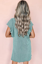 Donna con capelli ondulati biondi indossa un abito verde menta a coste con maniche corte volant, sfondo rosa. Moda estiva, abbigliamento casual.