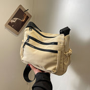 Borsa a tracolla beige con doppie cerniere nere, design moderno e funzionale. Accessorio moda unisex, ideale per viaggi e uso quotidiano.