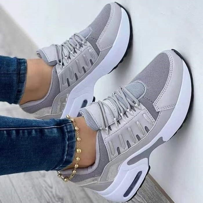 Scarpe da ginnastica grigie e bianche da donna, design moderno, suola ammortizzata, indossate con jeans. Sneakers casual comode e alla moda.