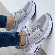 Scarpe da ginnastica grigie da donna, design moderno, suola bianca ammortizzata, indossate con jeans. Sneakers casual eleganti e comode.