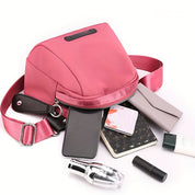 Borsa a tracolla rosa con tasca aperta, circondata da accessori: smartphone, portafoglio, rossetto, profumo, crema e taccuino. Accessori moda donna.