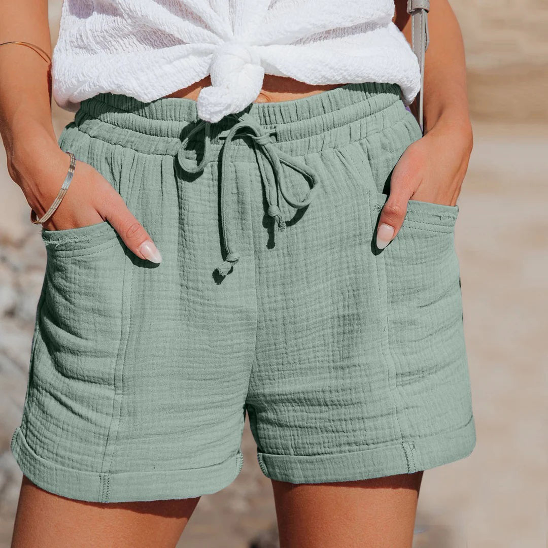 Shorts estivi donna in cotone verde salvia, con tasche e laccio in vita, abbinati a top bianco annodato. Moda casual estiva.