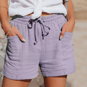 Shorts estivi da donna in cotone viola, con tasche e laccio in vita, abbinati a top bianco annodato. Stile casual e comodo per l'estate.