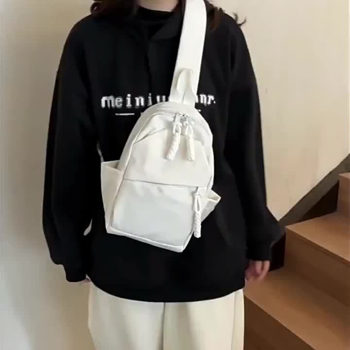Zaino bianco minimalista su persona con felpa nera, design moderno e compatto, ideale per moda casual e viaggi urbani. Accessorio unisex trendy.