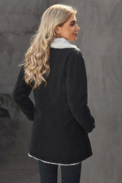 Donna di spalle con cappotto nero foderato in pelliccia sintetica bianca, capelli biondi ondulati, sfondo grigio. Moda invernale elegante.