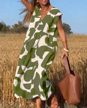 Abito estivo lungo verde e bianco con motivo astratto, indossato da una donna in un campo di grano, borsa marrone, giornata soleggiata.