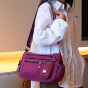 Borsa a tracolla viola da donna, design elegante con tasche multiple e cerniere, indossata su camicia bianca. Accessorio moda femminile.