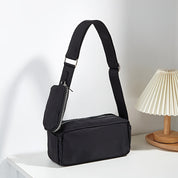 Borsa a tracolla nera su tavolo bianco, design moderno con tasca con zip, ideale per moda urbana e casual. Accessorio versatile ed elegante.