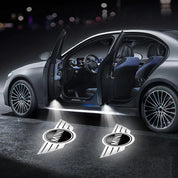 Auto grigia con portiere aperte, luci di cortesia proiettano logo MINI sul suolo. Design elegante, interni moderni, cerchi in lega.