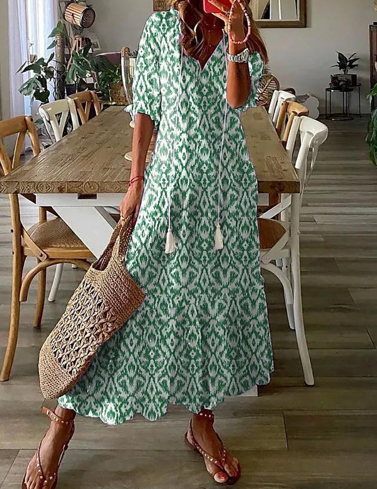 Abito lungo estivo verde con motivo etnico, maniche corte, indossato da donna con borsa di paglia. Perfetto per look casual e vacanze.